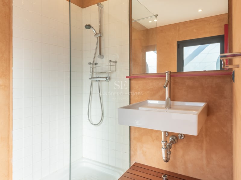 Modernt badrum med duschvägg i glas, vita kakelplattor och varma terracotta-färgade väggar med ett vitt tvättställ.