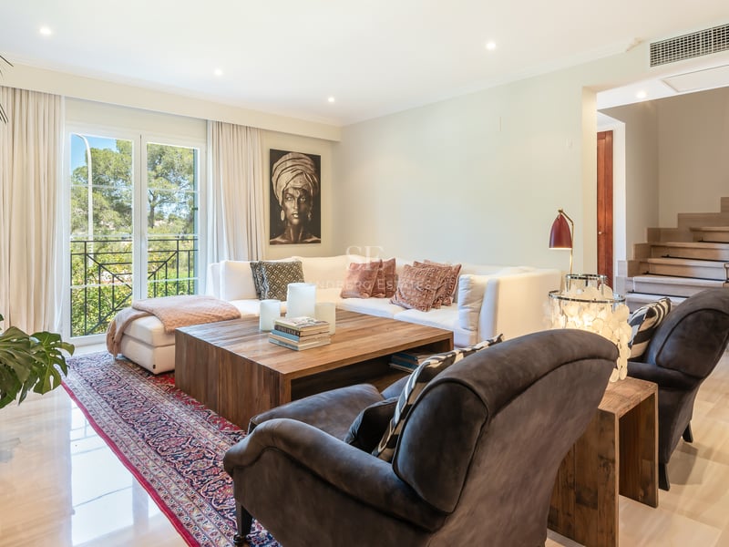 Sophisticated living room featuring a white sectional sofa, rustic wood table, marble floors, and garden views.