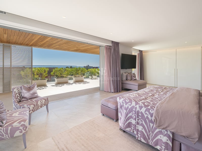 Luxuriöses Schlafzimmer mit Doppelbett, Zugang zur Holzterrasse und Meerblick durch große Glasschiebetüren.