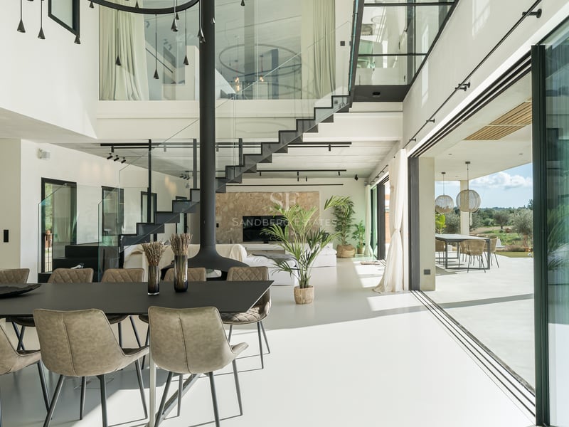 Modernt vardagsrum med öppen planlösning, svart svävande trappa, dubbel takhöjd och stora glaspartier.