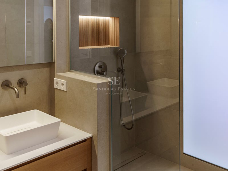 Salle de bain moderne avec vasque à poser, murs en pierre et douche vitrée avec niche en bois éclairée.