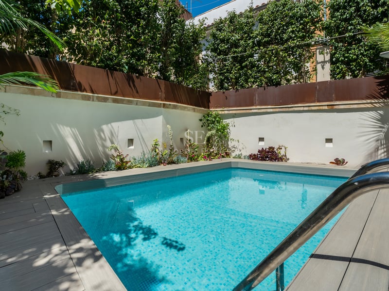 Piscine rectangulaire turquoise entourée d'une terrasse grise et de murs blancs avec des plantes tropicales luxuriantes.