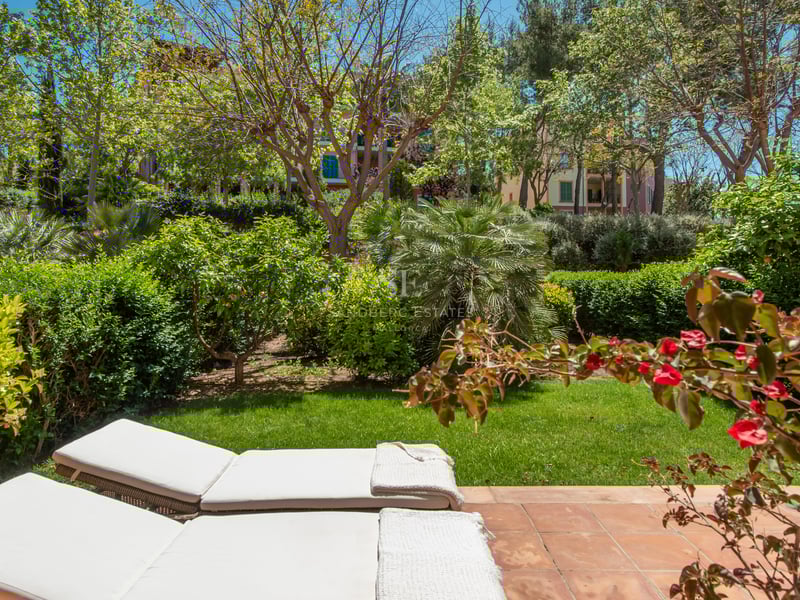 Two white sun loungers on a terracotta terrace overlooking a lush green garden with trees and flowering plants.