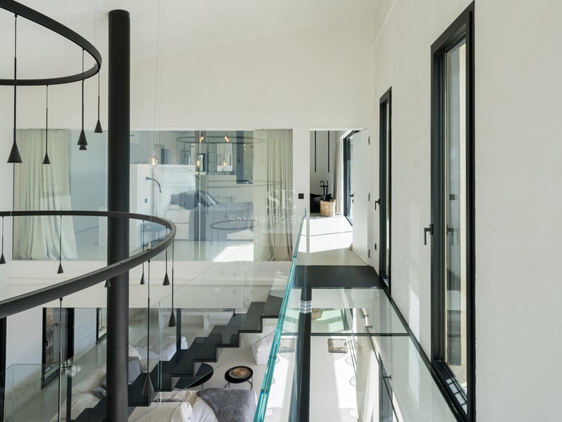 Modern hall med gångbro i glas, svart trappa och stora fönsterpartier i en lyxig villa.