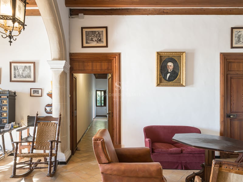 Salon classique avec meubles anciens, sol en terre cuite, canapé en velours rouge et portraits aux murs.