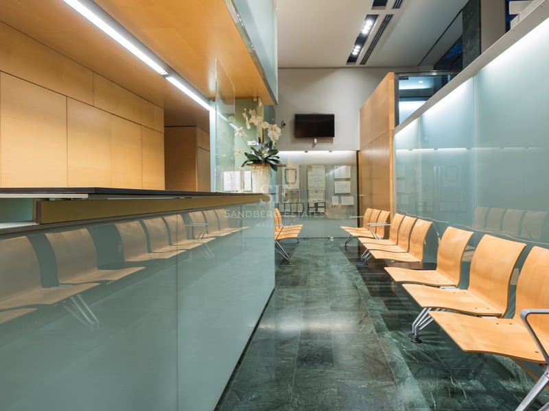 Espace de réception moderne avec cloisons en verre dépoli, sièges en bois clair et sol en marbre vert foncé.