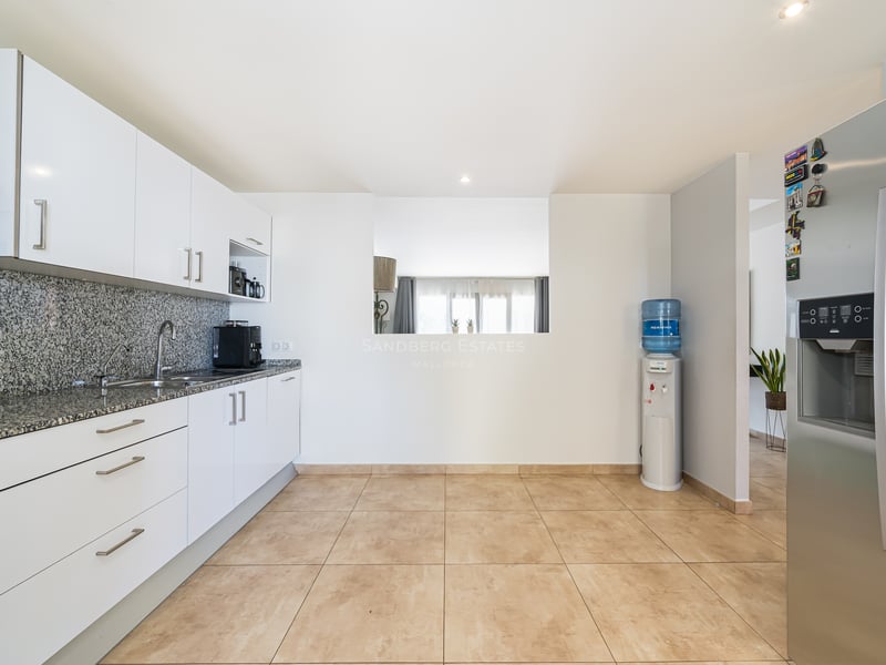 Ett modernt kök med vita skåp, spräckliga bänkskivor i granit och ett stort kylskåp i rostfritt stål.