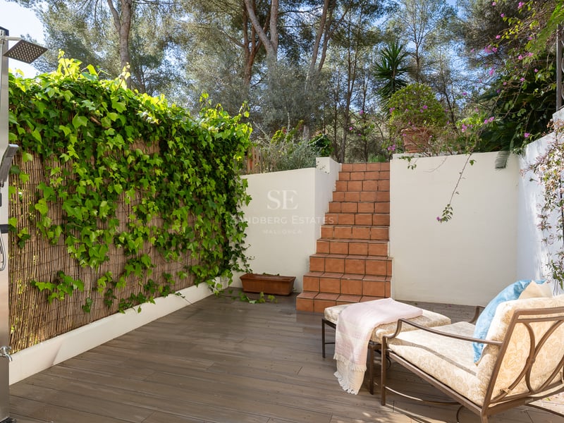 An outdoor terrace featuring a modern stainless steel shower, terracotta steps, a lounge chair, and a green ivy wall.