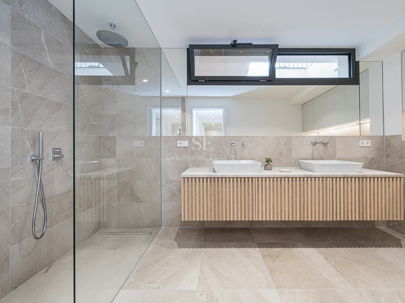 Modern bathroom featuring a walk-in glass shower, sand-colored stone tiles, and a floating wood double vanity.