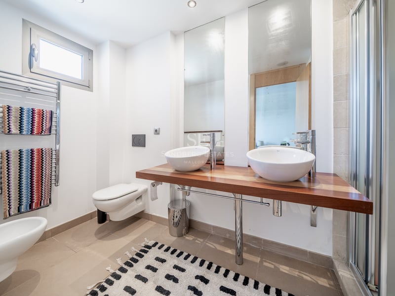 Salle de bain lumineuse avec plan de toilette en bois, deux vasques blanches, sèche-serviettes et grands miroirs.