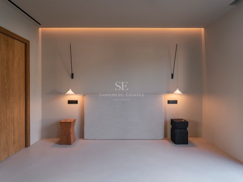 Tête de lit rembourrée entre des suspensions et des tabourets en bois sous un éclairage chaleureux et indirect.