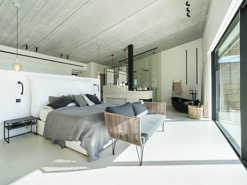 Modernt huvudsovrum med grå säng, betongtak och integrerat svart fristående badkar.