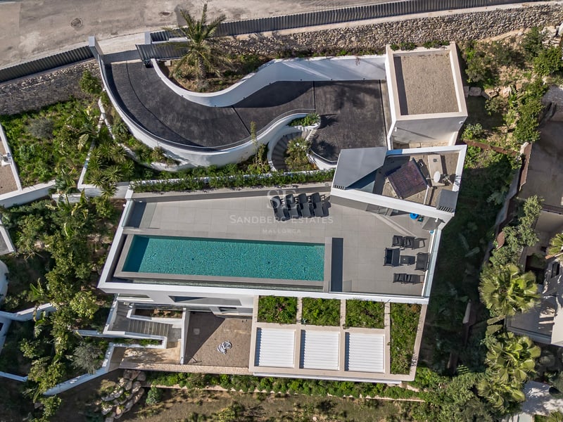 Vue aérienne d'une villa moderne avec piscine rectangulaire, terrasse avec chaises longues et rampe d'accès courbe.