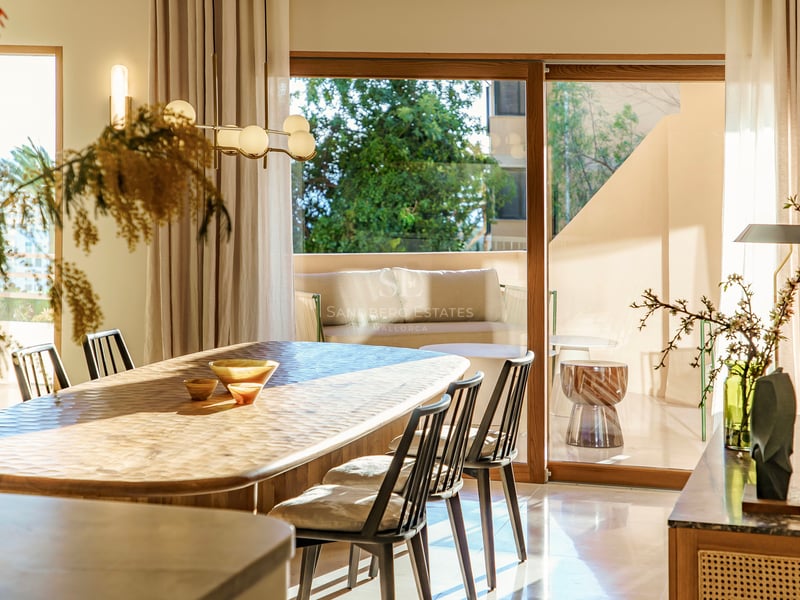 Sonnendurchflutetes Esszimmer mit handgeschnitztem Holztisch und schwarzen Stühlen vor großen Glasschiebetüren.
