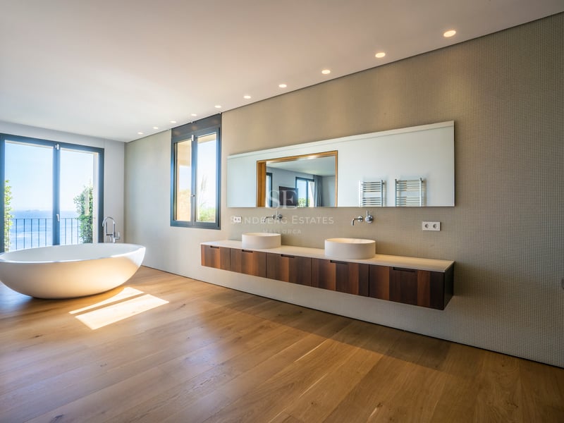 Modernes Badezimmer mit freistehender Badewanne, Eichenparkett, Doppelwaschtisch und Meerblick durch Glastür.