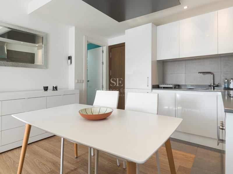 Cuisine moderne lumineuse avec des placards blancs, une crédence grise et une table à manger blanche.