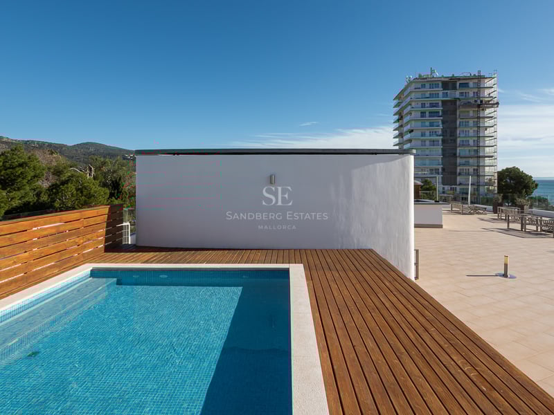 Piscine moderne sur le toit avec terrasse en bois, vue sur la mer et les montagnes sous un ciel bleu clair.