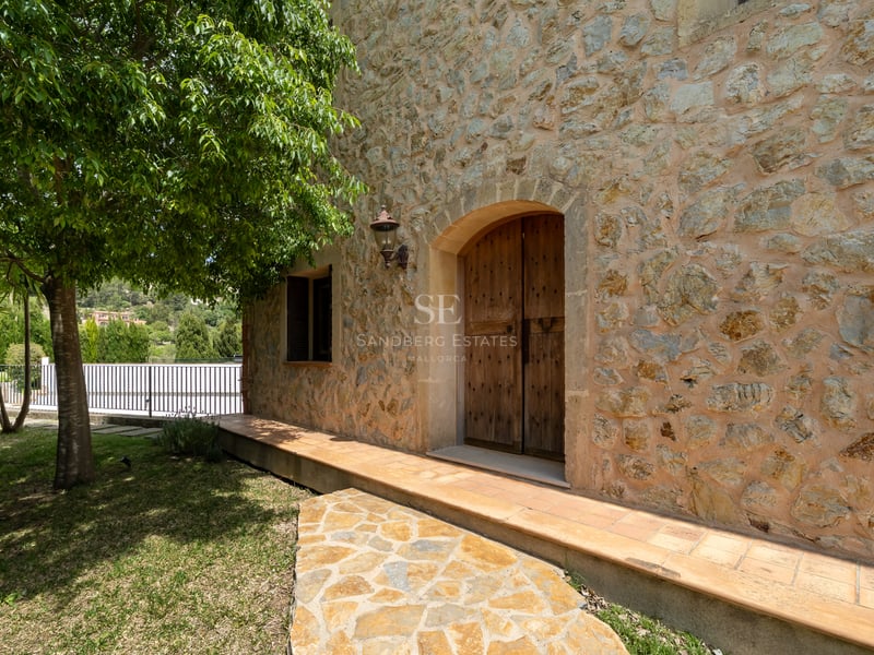 Portes doubles en bois voûtées dans une façade en pierre naturelle avec une lanterne en fer et un chemin ombragé.