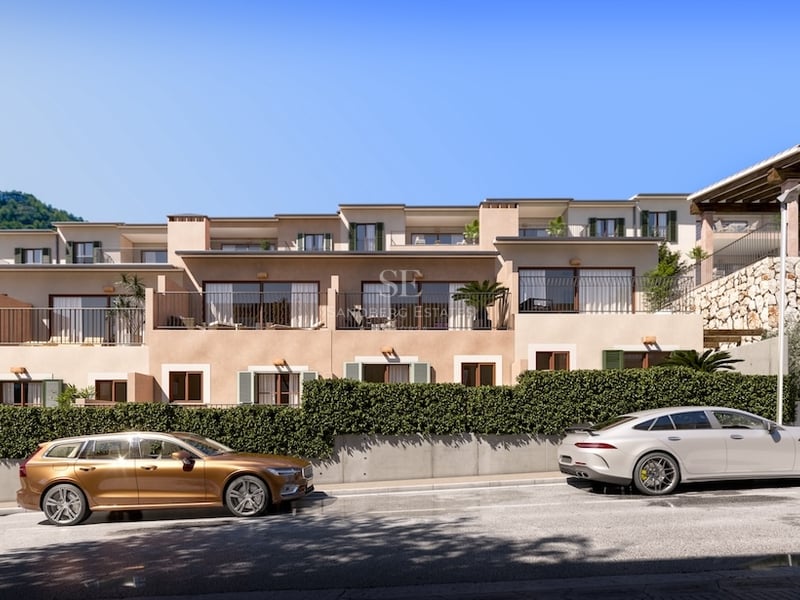Exterior view of modern multi-level Mediterranean residences with stone walls, balconies, and cars parked on the street.