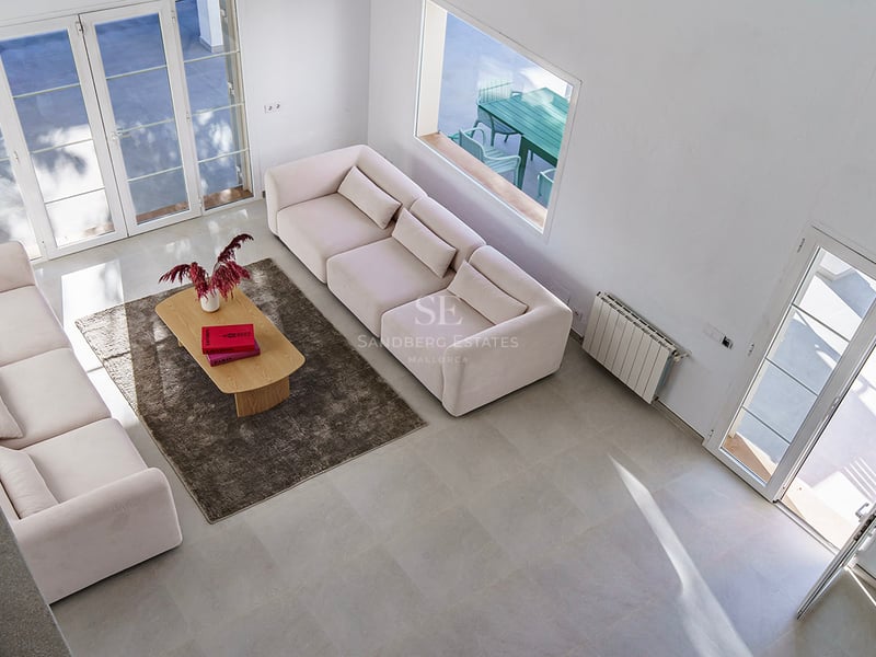 Upphöjd vy av ett ljust vardagsrum med cremefärgade soffor, soffbord i trä och stora glasdörrar mot en terrass.