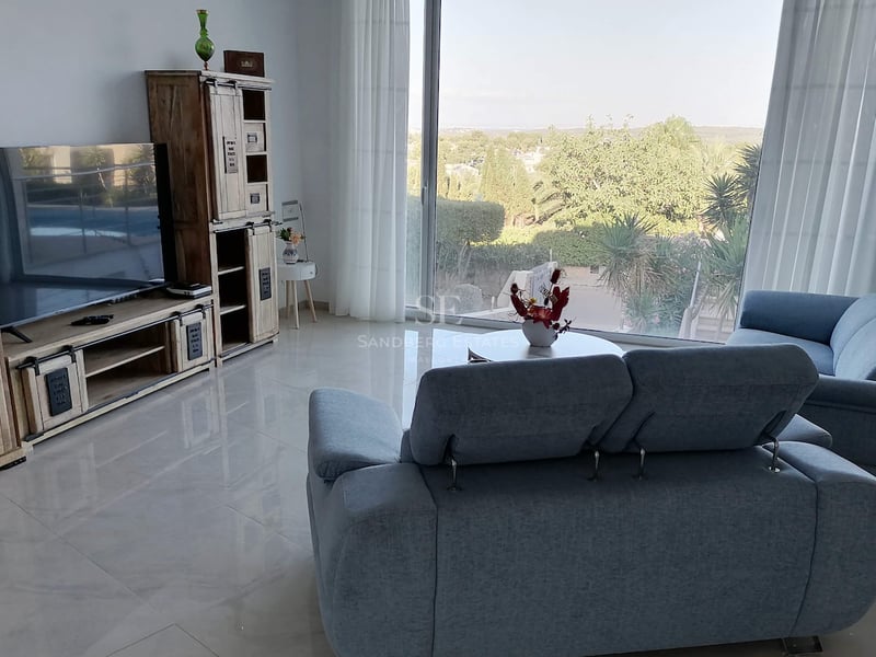 Salon moderne avec canapés en tissu gris, sol en grès poli et grande baie vitrée donnant sur la verdure.