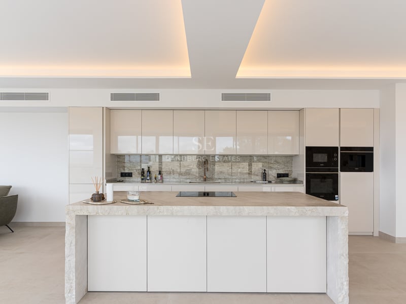 Minimalistische weiße Küche mit Marmorinsel und indirekter Deckenbeleuchtung in einer Luxusvilla.