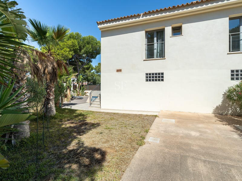 Exteriör av en tvåvåningsvilla i krämvitt med tegeltak och palmer under en klarblå himmel.