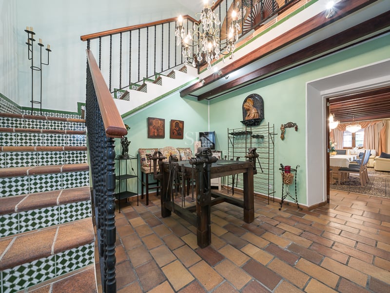 Hall d'entrée spacieux avec sol en terre cuite, escalier en fer forgé orné d'azulejos et poutres apparentes.
