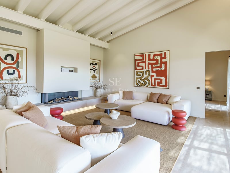 Helles Wohnzimmer mit hohen Balkendecken, modernem Kamin, weißen Sofas und abstrakter Wandkunst.