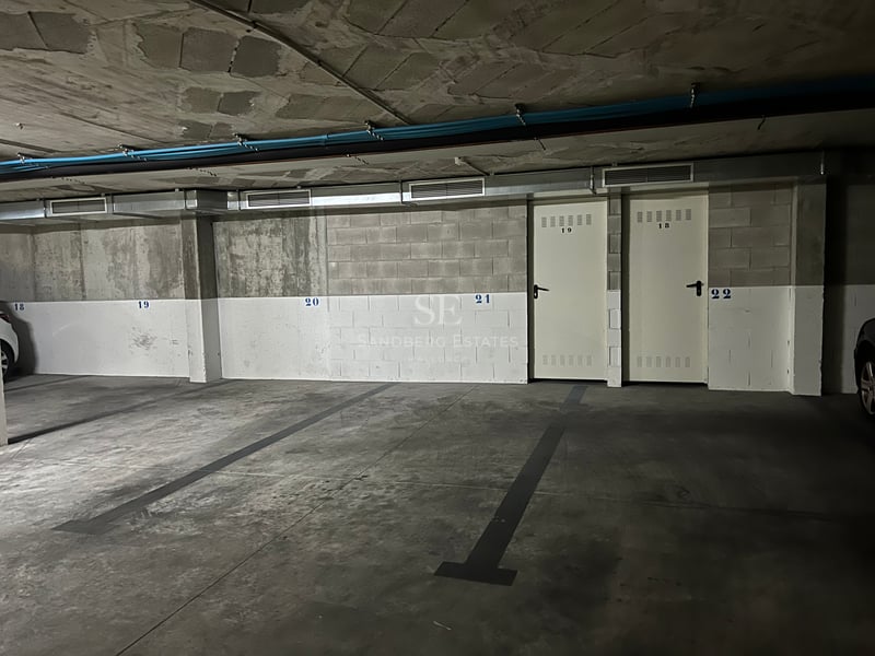 Garage souterrain avec sol en béton, places numérotées et portes de rangement en métal blanc.