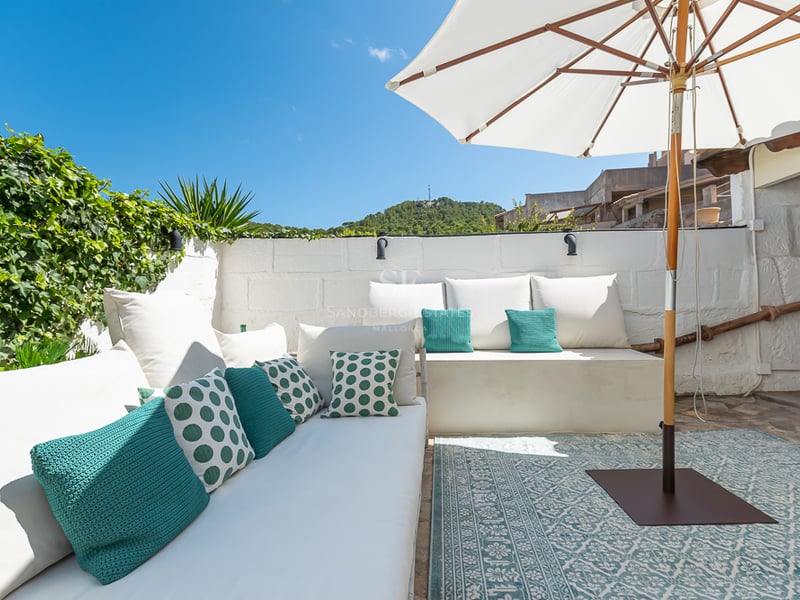 Terrasse privée en pierre blanche avec banquettes intégrées, coussins colorés, grand parasol et vue sur la montagne.