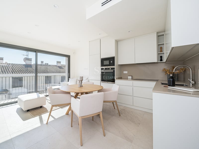 Bright kitchen with white cabinetry, wood dining table, and large glass doors overlooking traditional rooftops.