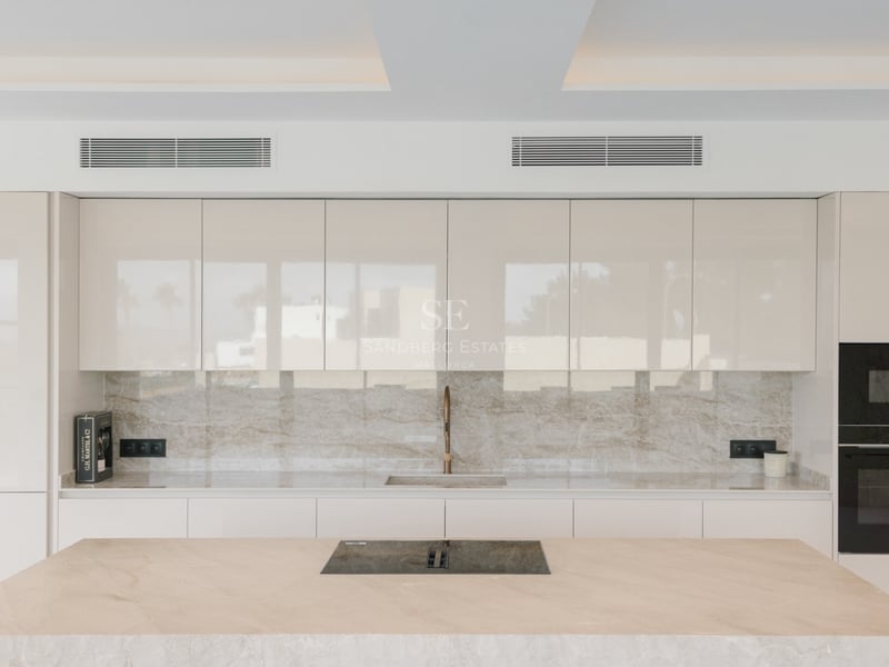 Minimalistische Küche mit cremefarbenen Glanzschränken, Marmorinsel und integrierten High-End-Geräten.