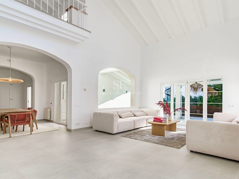 Rymligt vitt vardagsrum med högt i tak, bjälkar, beige soffor och matplats genom en rundbåge.