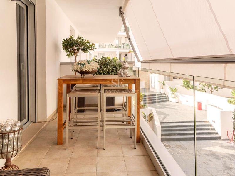 Moderne Terrasse mit hohem Holztisch, Hockern, weißer Markise und Glasgeländer mit Blick auf den Innenhof.