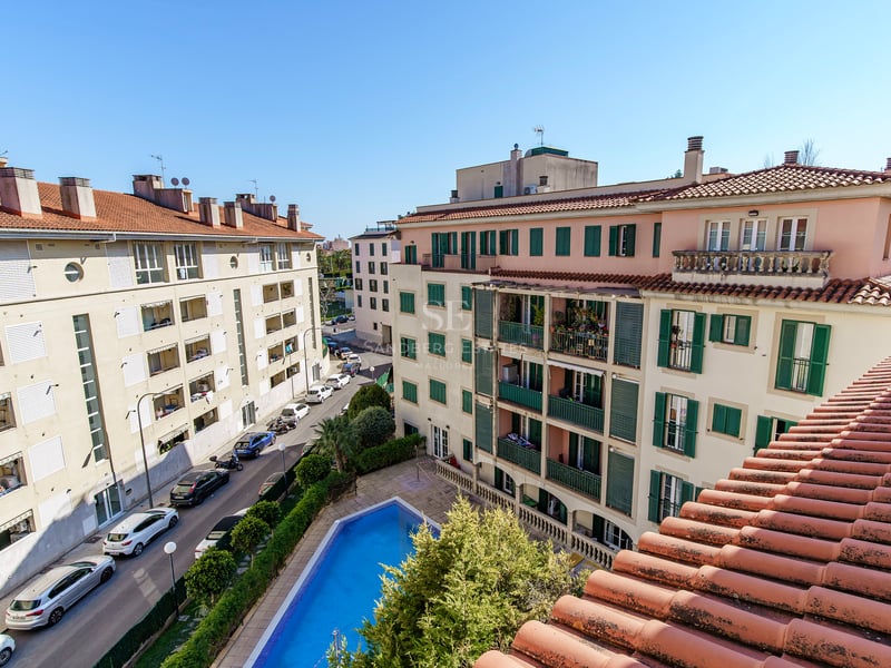 Flygvy över en blå pool omgiven av medelhavsbyggnader med gröna fönsterluckor och terrakottatak.