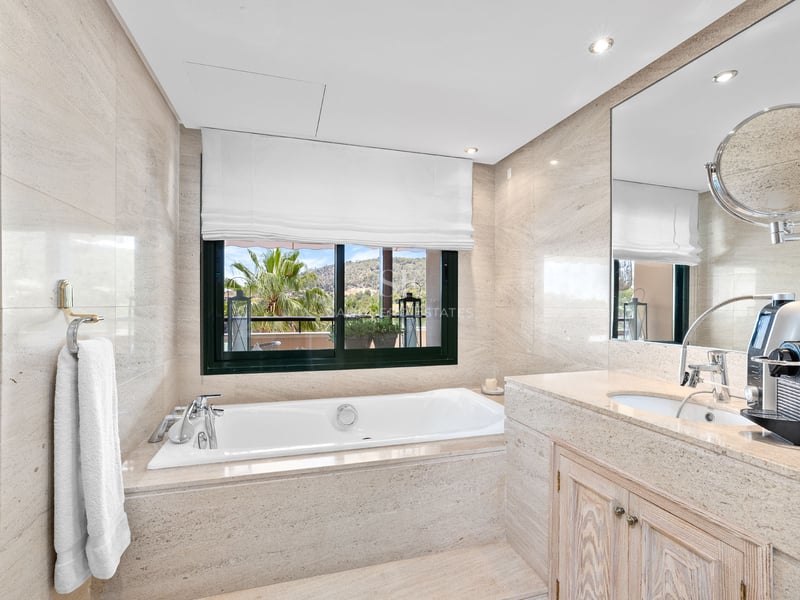 Salle de bain principale élégante avec baignoire en pierre, grande fenêtre avec vue et vasque en marbre.