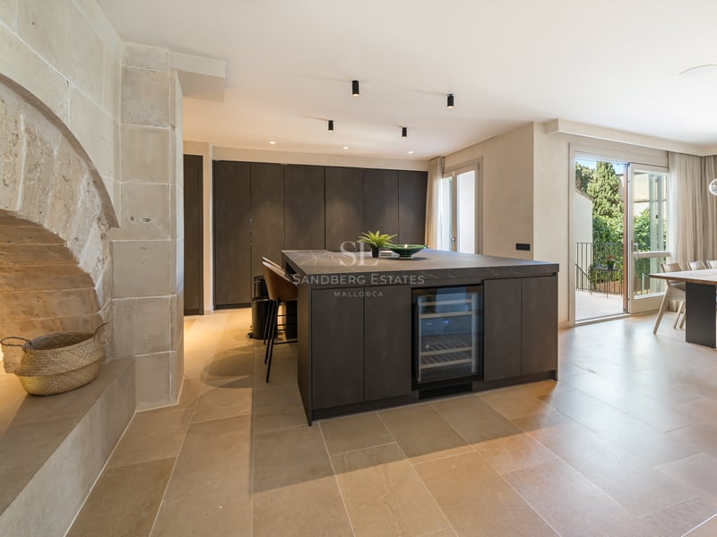 Cuisine haut de gamme avec îlot sombre, cave à vin, arche en pierre naturelle et salle à manger lumineuse.