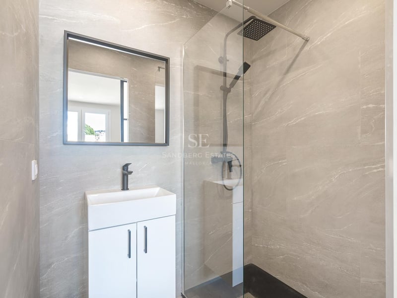 Modernes Badezimmer mit grauen Steineffekt-Fliesen, Glasduschwand, Regenduschkopf und mattschwarzen Armaturen.