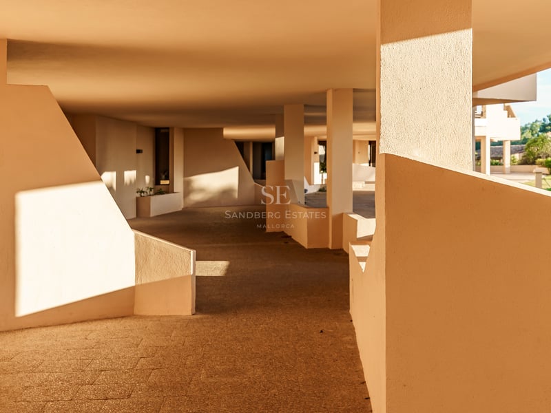 Schattiger Außenweg mit beigen geometrischen Wänden und Steinboden bei warmem Sonnenlicht und scharfen Schatten.