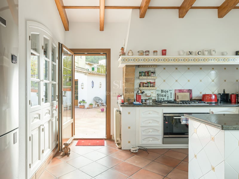 Kitchen featuring exposed wood beams, terracotta floors, and an open door leading to a sunny courtyard.