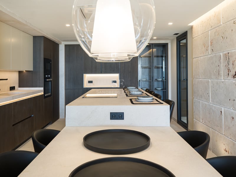 Cuisine moderne avec un grand îlot en pierre, des armoires en bois sombre et un mur en pierre naturelle texturée.