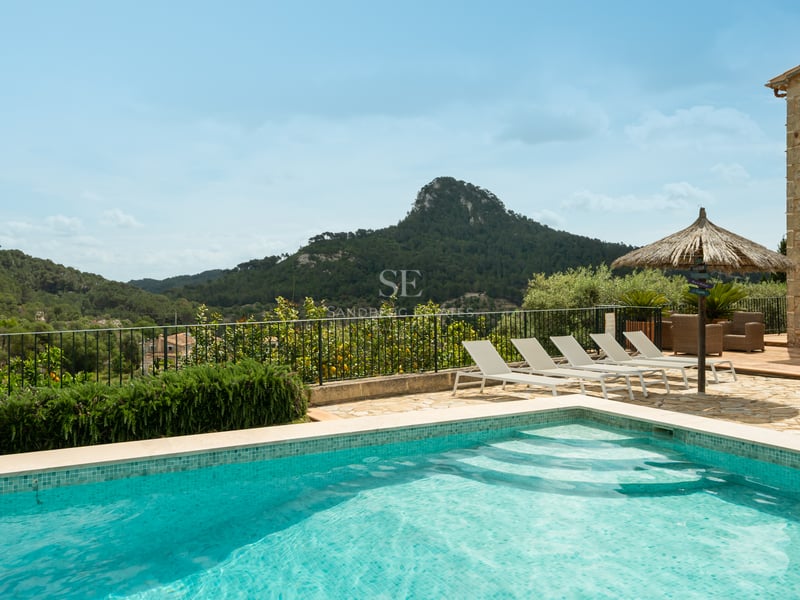 Piscine extérieure avec chaises longues sur une terrasse en pierre, surplombant un paysage de montagne verdoyant.