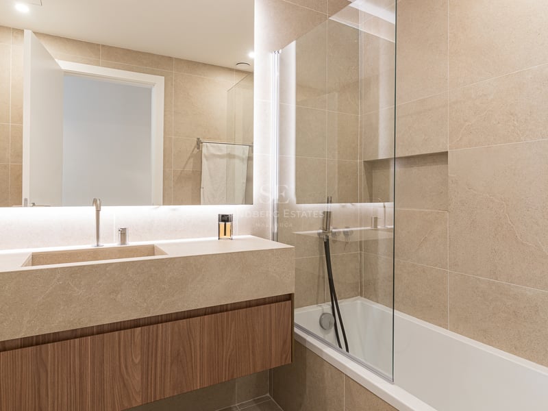 Modern bathroom featuring a floating wood vanity, large-format stone tiles, and a backlit mirror.