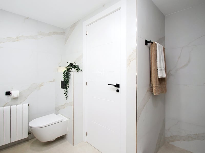 Modernt badrum med stora plattor i marmoreffekt, vägghängd toalett och detaljer i mattsvart.