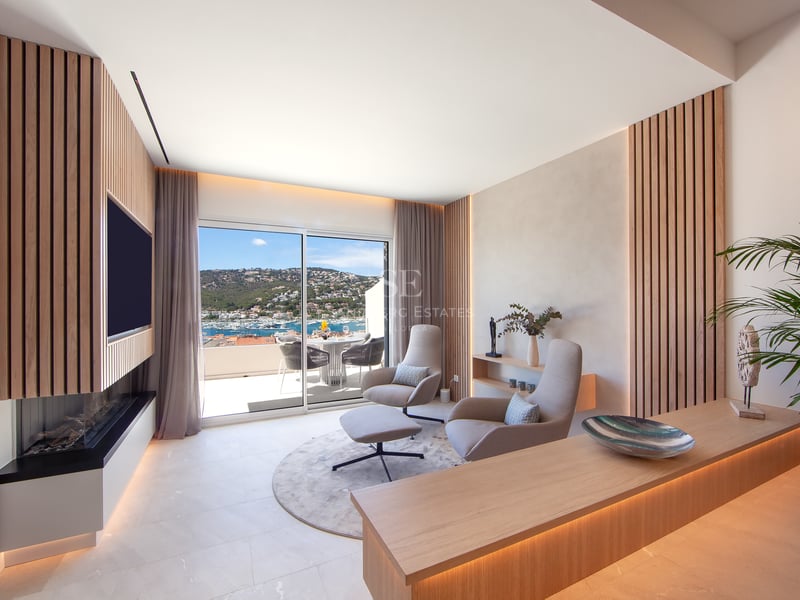 Salon moderne avec lattes de bois, fauteuils design et vue panoramique sur le port à travers des baies vitrées.