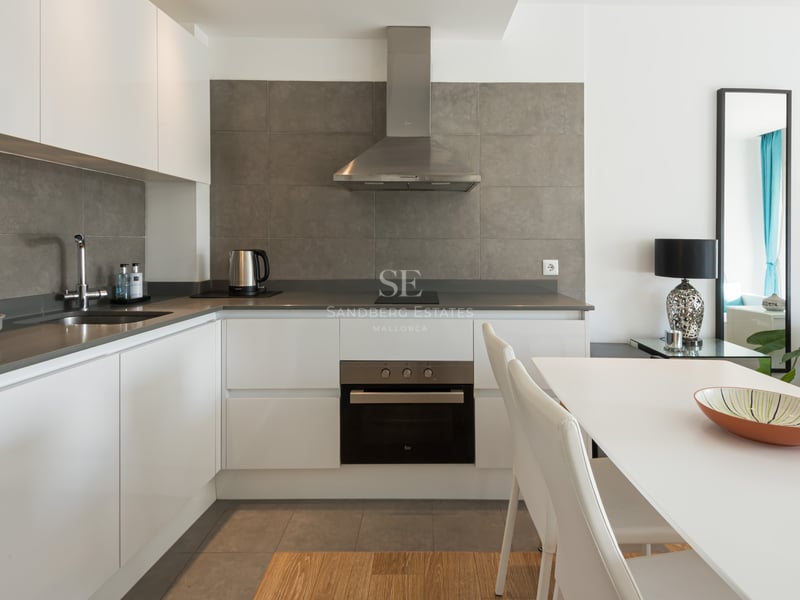 Cuisine blanche moderne avec crédence grise, appareils en inox et table à manger blanche.