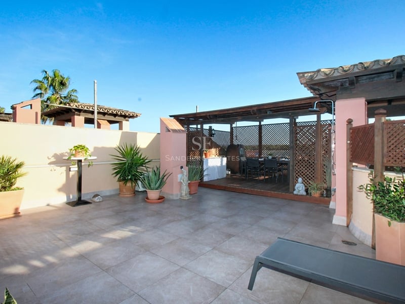 Solsida terrass med grått klinkergolv, träpergola, terrakottafärgade väggar och medelhavsväxter i krukor.