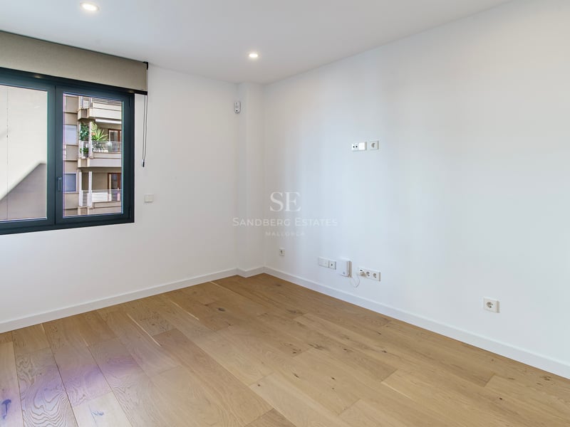 Pièce vide et lumineuse avec parquet en bois clair, murs blancs et une grande fenêtre avec store.