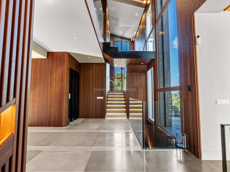 Hall d'entrée moderne avec murs en bois à lattes, escalier en verre avec éclairage LED et grandes baies vitrées.
